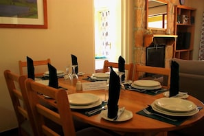 A dining table set for six with wooden chairs, a sign thanking guests for choosing Riverbend as their holiday destination, and a stone wall with a fireplace. - Riverbend Chalets (Drakensberg Gardens)