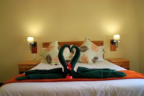 A hotel room with a neatly made bed, two nightstands, and wall-mounted lamps. - Riverbend Chalets (Drakensberg Gardens)