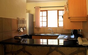 A kitchen with a marble countertop, a sink, a window with curtains, and a telephone on the counter.