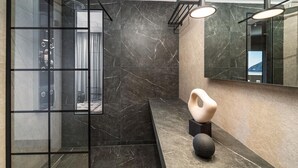 A modern bathroom with a glass shower enclosure, a marble-tiled wall, and a large mirror. - San Giovanni Luxury Studios (Lefkada)