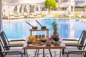 Un área de comedor junto a la piscina con una mesa preparada para el desayuno, con vista a una pileta.