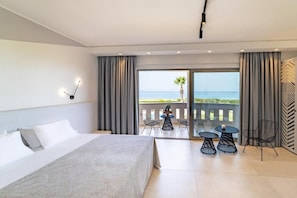 A hotel room with a large bed, a balcony with a table and chairs, and a view of the sea. - San Giovanni Luxury Studios (Lefkada)