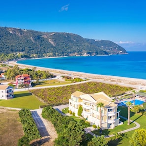 Un hotel costero con varias construcciones, una piscina y vistas al mar y a las colinas.