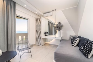 A modern living room with a sofa, a chair, a dining table, and a large window with a view. - San Giovanni Luxury Studios (Lefkada)