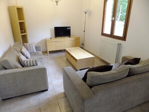 A living room with a sofa set, a TV, a lamp, and a window. - Le Clos Gentiane [vr] (Saint-Etienne)