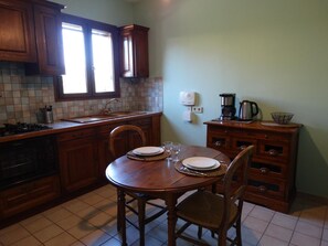 A kitchen with wooden cabinets, a tiled backsplash, a dining table with chairs, and a coffee maker.