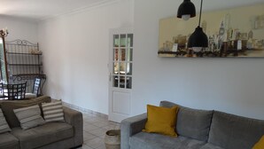 A living room with two sofas, a dining table with chairs, a lamp, and a cityscape painting on the wall. - Le Clos Gentiane [vr] (Saint-Etienne)