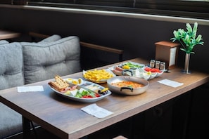 Ruokapöytä, jossa on erilaisia ruokia, kuten leipää, salaattia ja kattilallinen valmista ruokaa, modernissa sisustuksessa.