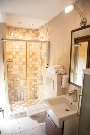 Un baño moderno con ducha acristalada, lavamanos blanco y espejo.