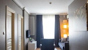 Ein Hotelzimmer mit Holzboden, einem Sessel, einer Couch, einem Fernseher und einem Fenster mit Vorhängen.