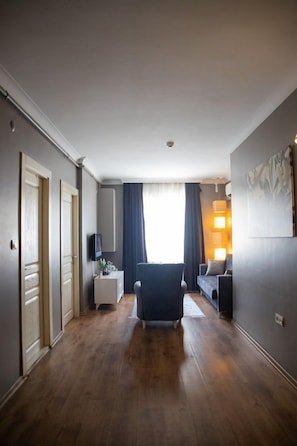 Hotellihuone, jossa on puulattia, tuoli, sohva, televisio ja ikkuna, jossa on verhot.