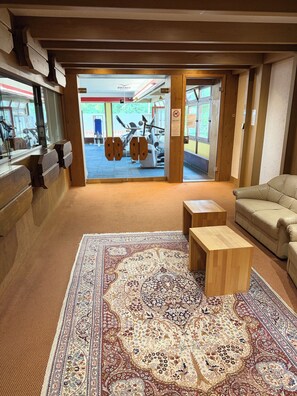 A room with a large patterned rug, a wooden bench, a leather sofa, and a view of an exercise area with cardio machines. - Schluchsee Dream in the Black Forest (Schlochsee)