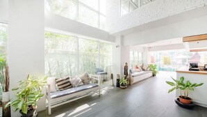 Uma sala de estar ampla com pé direito alto, grandes janelas e um espaço de estar com sofá e um banco.