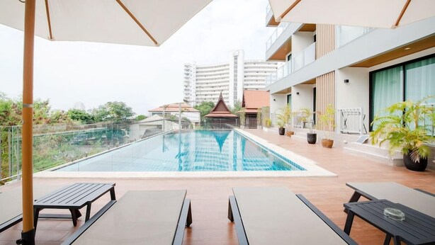 Piscina no terraço com espreguiçadeiras e guarda-sóis, cercada por plantas em vasos e vista para um edifício tradicional.
