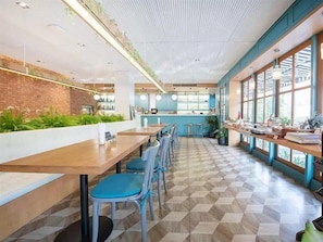 Una cafetería con mesas de madera largas, sillas azules y un piso a cuadros.