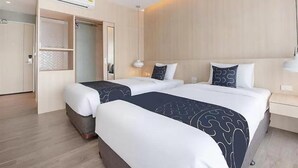 Quarto de hotel com duas camas, um guarda-roupa e uma mesa de cabeceira.