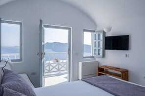 A bedroom with a bed, a television, a window, and a view of the sea. - Oia Spirit Suites Adults Only (Santorini)