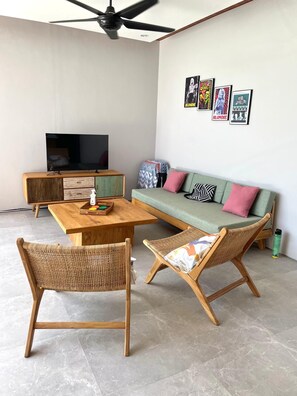 A modern living room with a sofa, two wicker chairs, a coffee table, and a television. - Rumah Melissa Modern Boho 3BR Villa in Sanur (Denpasar selatan)
