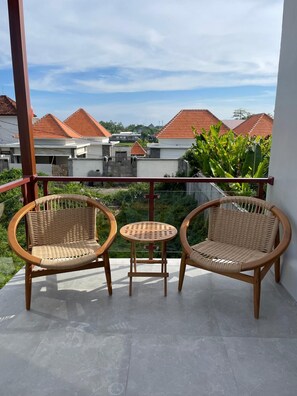 A balcony with two wicker chairs and a small round table, overlooking a residential area with red-roofed houses. - Rumah Melissa Modern Boho 3BR Villa in Sanur (Denpasar selatan)
