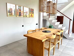 Uma sala de jantar com mesa e cadeiras de madeira, escada e obras de arte nas paredes.