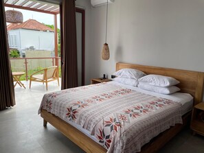Quarto com cama de madeira, roupa de cama branca, luminária pendente e vista para o exterior.