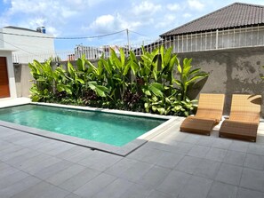 A swimming pool with a tiled deck, surrounded by lush greenery and a white fence. - Rumah Melissa Modern Boho 3BR Villa in Sanur (Denpasar selatan)