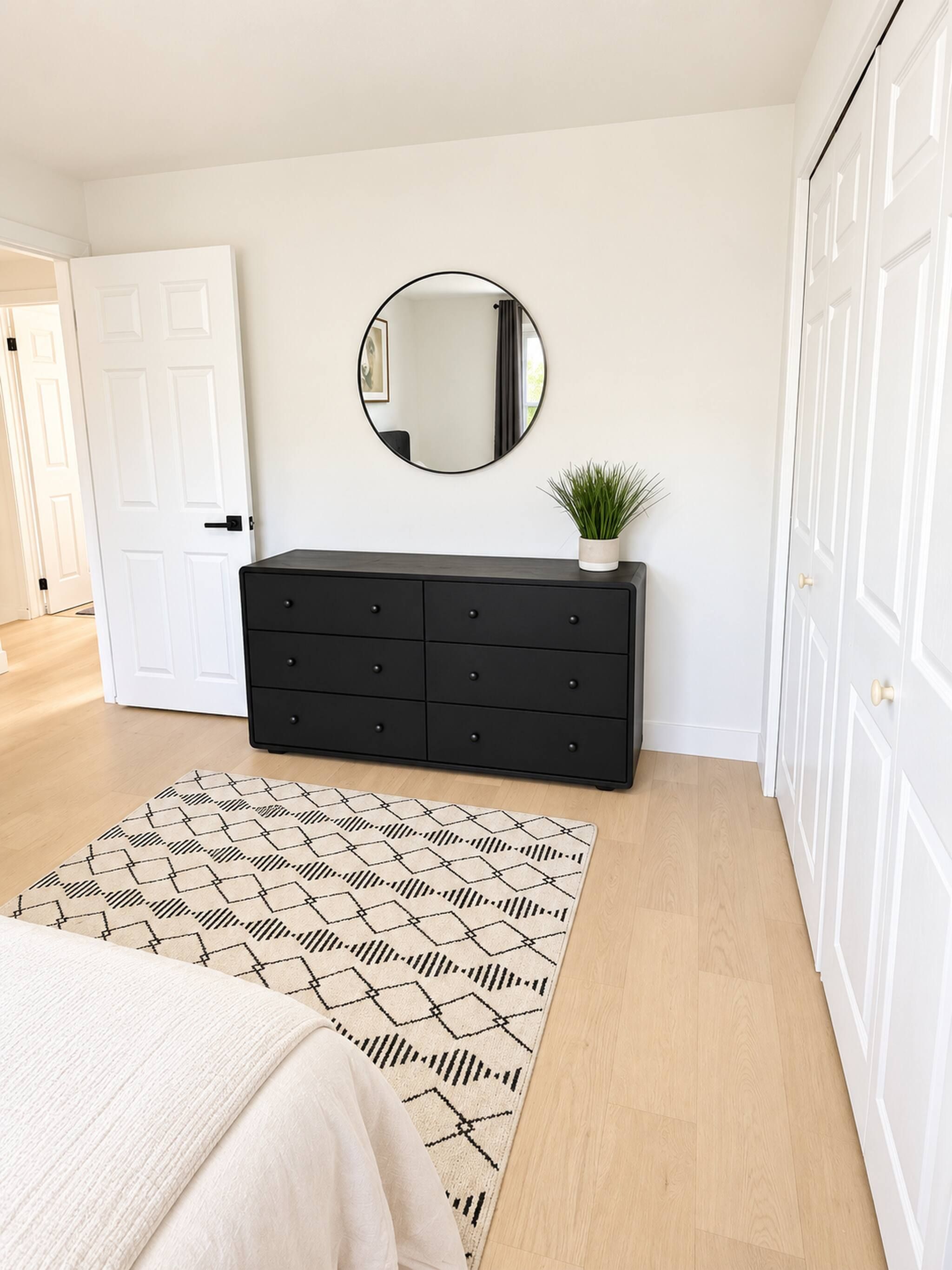 Un dormitorio con cama, cómoda, espejo y alfombra estampada.