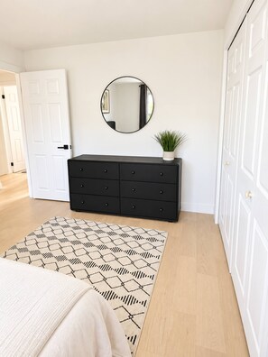 Un dormitorio con cama, cómoda, espejo y alfombra estampada.
