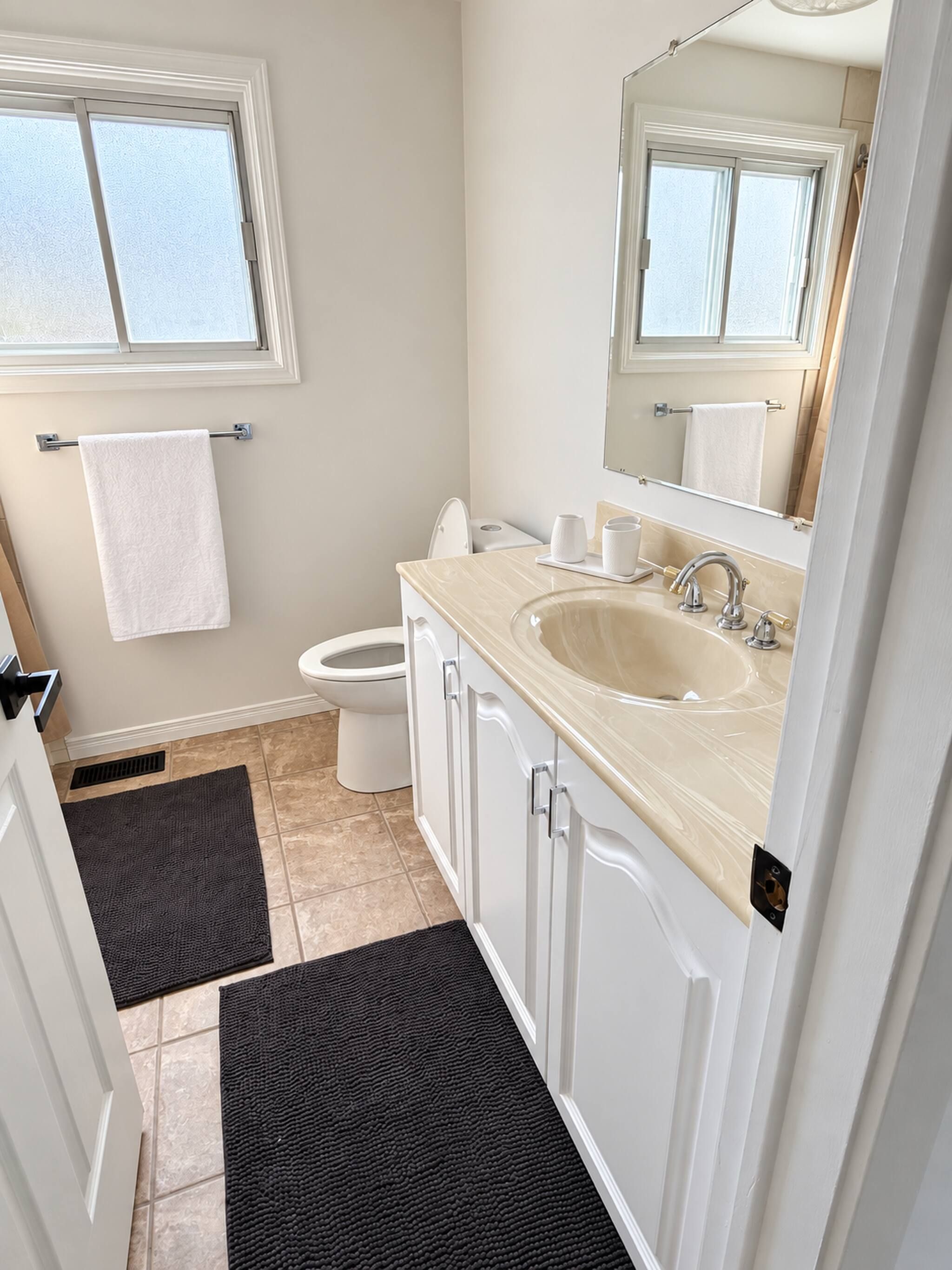 A bathroom with a toilet, sink, and mirror. There are two towels hanging on the wall.