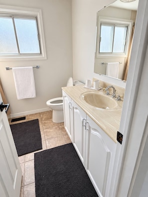 A bathroom with a toilet, sink, and mirror. There are two towels hanging on the wall. - Modern 3BR Home Near Cheo & General Hospital (Ottawa)