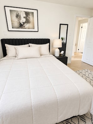 A neatly made bed with a black headboard, a bedside table with a lamp, and a framed artwork on the wall. - Modern 3BR Home Near Cheo & General Hospital (Ottawa)