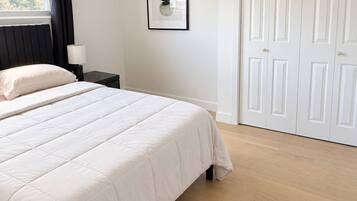 Habitación de hotel con cama, mesita de noche, lámpara, una obra de arte abstracta enmarcada y un juego de puertas blancas.