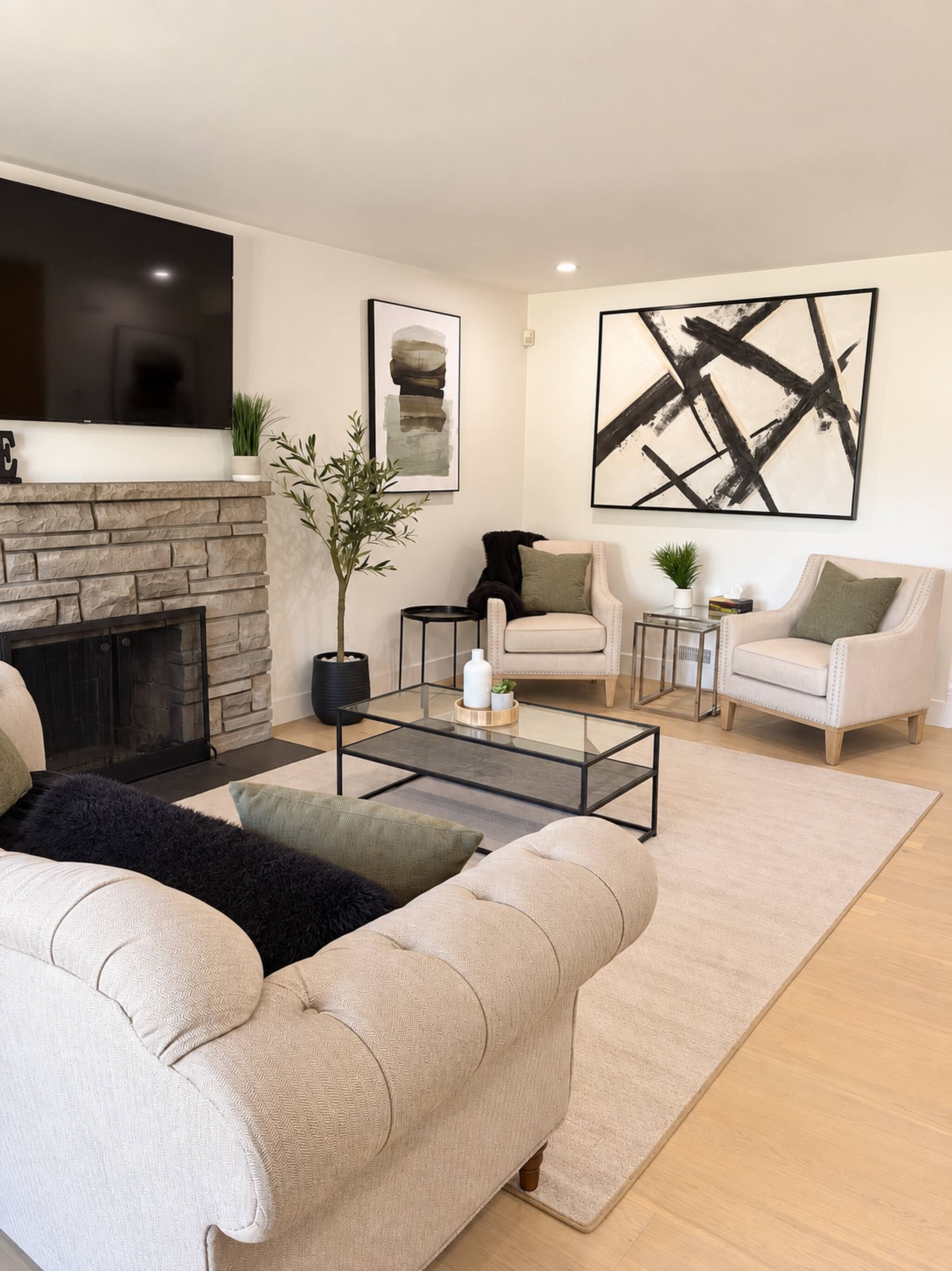 A modern living room with a fireplace, a flat-screen TV, a coffee table, and two armchairs.