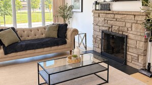 A living room with a sofa, a glass coffee table, a fireplace, and a large window. - Modern 3BR Home Near Cheo & General Hospital (Ottawa)
