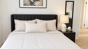 Un dormitorio con una cama, una mesita de noche, una lámpara, un cuadro en la pared y un espejo.