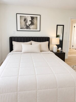 A bedroom with a bed, a nightstand, a lamp, a framed picture on the wall, and a mirror. - Modern 3BR Home Near Cheo & General Hospital (Ottawa)