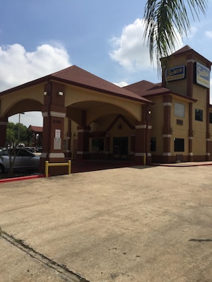 A hotel with a covered entrance, a parking lot, and a sign for 'Scotts Inn & Suites.' - Scottish Inns (Houston)