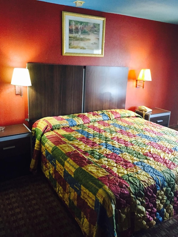 A hotel room with a large bed, two bedside tables, a nightstand, a lamp, and a painting on the wall.