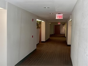 A hotel hallway with a carpeted floor, white walls, and an exit sign.