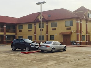 A hotel with a red roof and yellow walls, two cars parked in front, and a clear sky. - Scottish Inns (Houston)