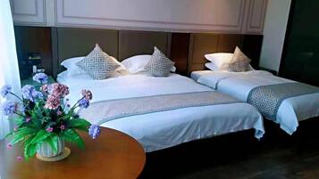 A hotel room with two beds, a round wooden table with a vase of flowers, and a large window.