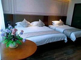 Habitación de hotel con dos camas, una mesa redonda de madera y un florero con flores, además de un ventanal grande.