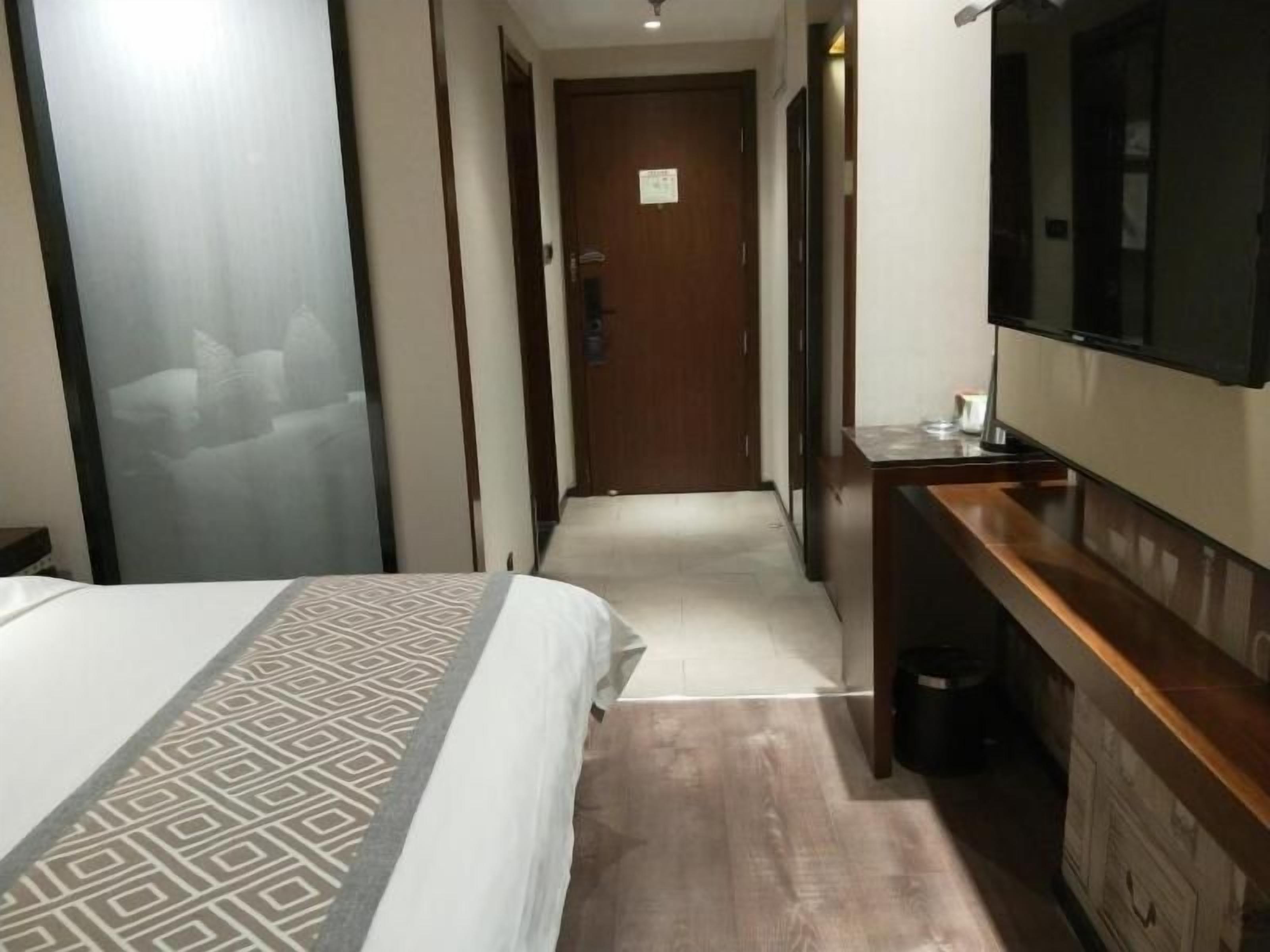 A hotel room with a bed, a TV, a wooden dresser, and a door leading to another room.