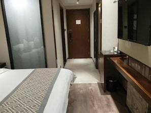 A hotel room with a bed, a TV, a wooden dresser, and a door leading to another room. - Gem Huainan Tianjia 'an District Chaoyang East Road Wanda Plaza Hotel (Huainan)