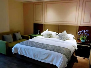 Quarto de hotel com uma cama, um sofá, uma mesa de cabeceira e um vaso com flores.