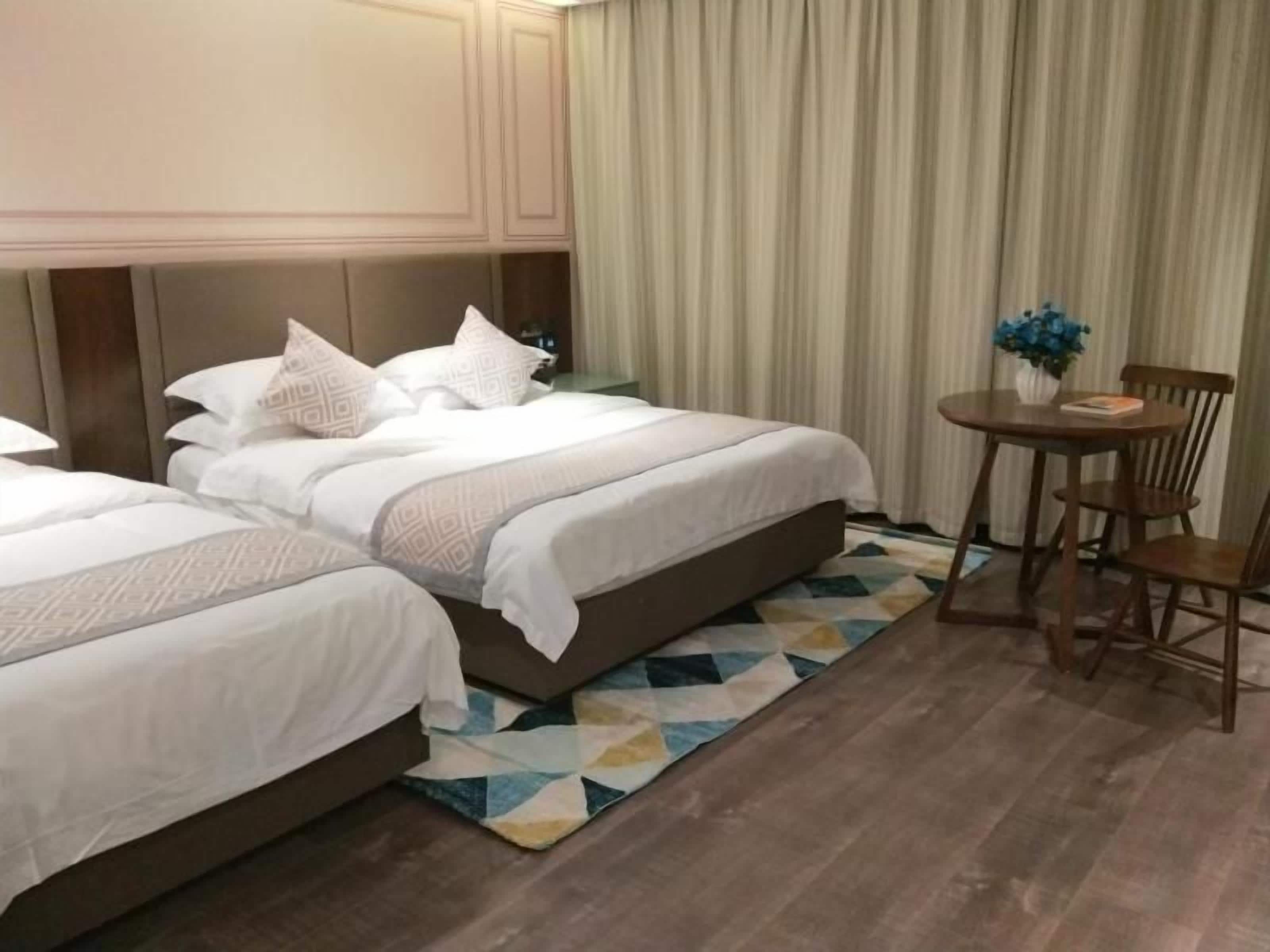 Habitación de hotel con dos camas, una mesita con sillas y una alfombra estampada.