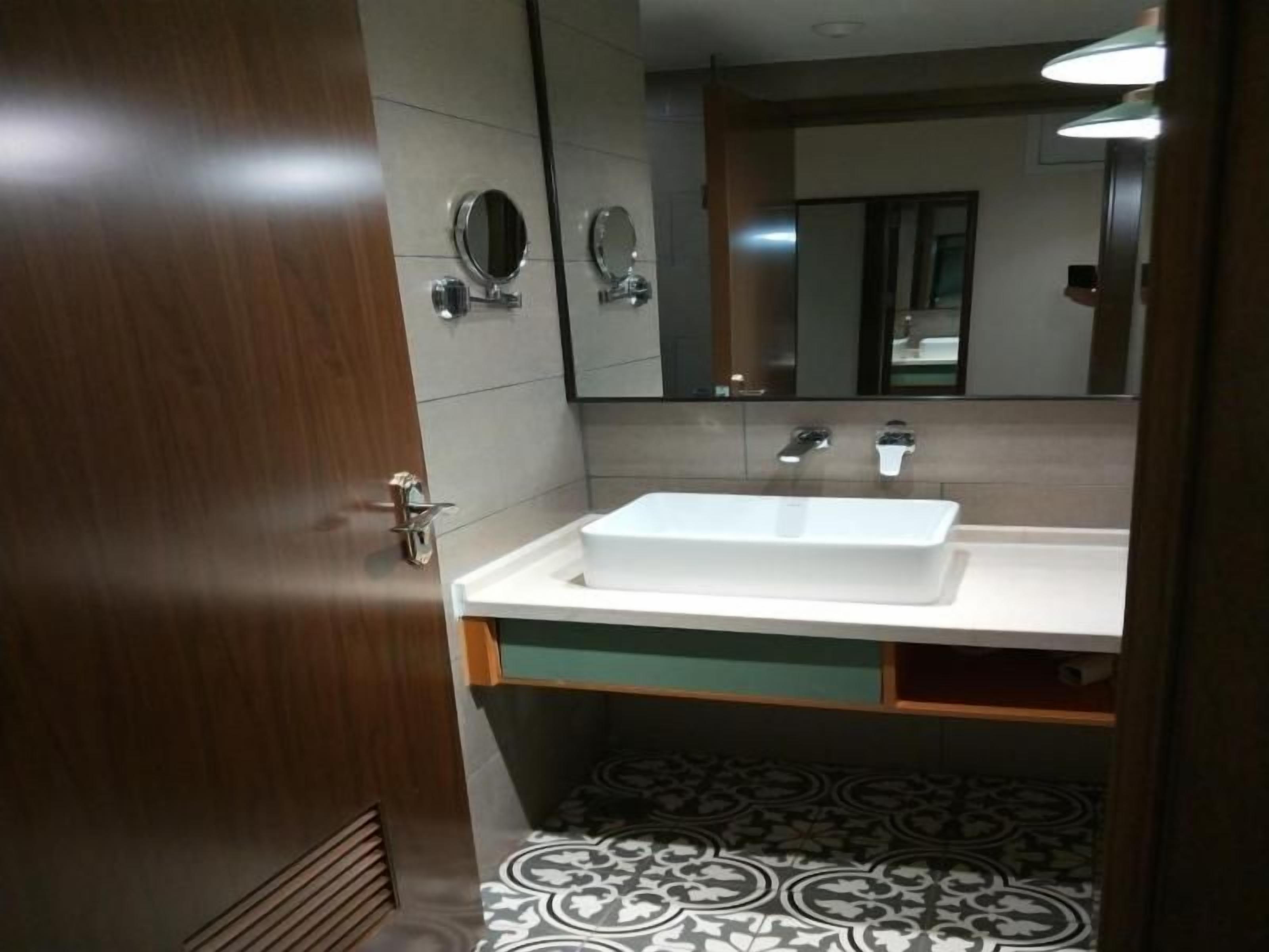 A bathroom with a white sink, two mirrors, and a patterned floor.