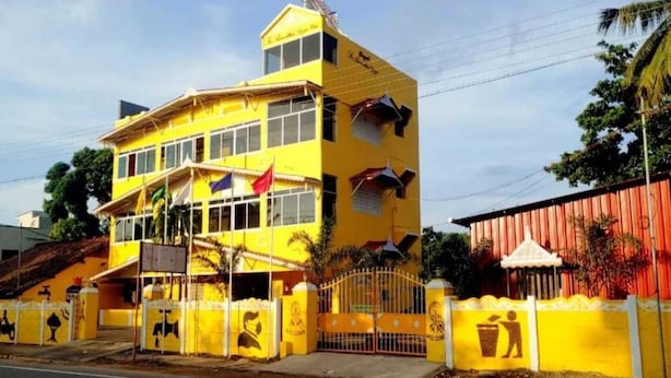 A yellow multi-story building with a flat roof, a gated entrance, and a flagpole. - Collection O Thirukadaiyur Bus Terminal (Tarangambadi)