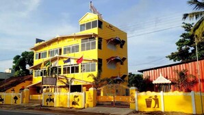 A yellow multi-story building with a flag on top, a gated entrance, and a fenced area with waste bins. - Collection O Thirukadaiyur Bus Terminal (Tarangambadi)