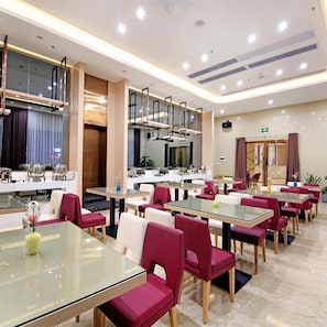 A modern dining area with glass tables and red upholstered chairs, featuring a central kitchen and a glass partition. - Lavandelavande Hotel (Zhongshan)